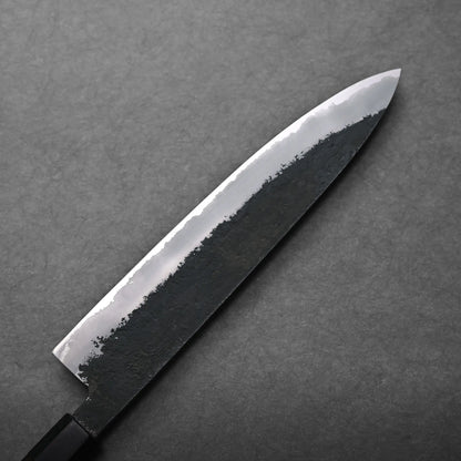 A close-up of a Japanese chef's knife with a black handle and sharp, polished blade featuring a dark textured pattern near the edge, set against a gray background.