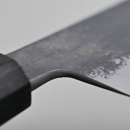 Close-up of the choil finish of the chef's knife against a plain background.