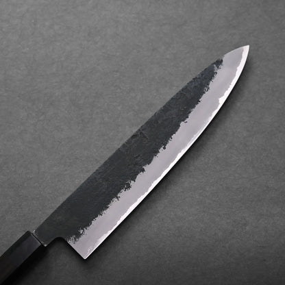 A close-up of a Japanese chef's knife with a dark, textured blade and a straight-edged handle, placed on a gray surface.