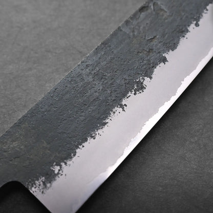 Close-up view of a Japanese chef's knife blade highlighting the contrast between its rough, dark, textured upper section and the smooth, polished lower edge against a dark background.