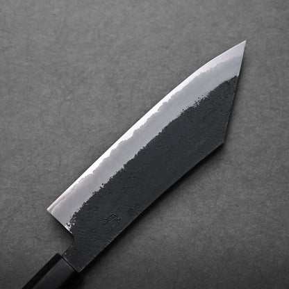 A close-up view of a Japanese-style hakata knife with a black, textured blade and sharp, pointed tip, placed on a gray surface.