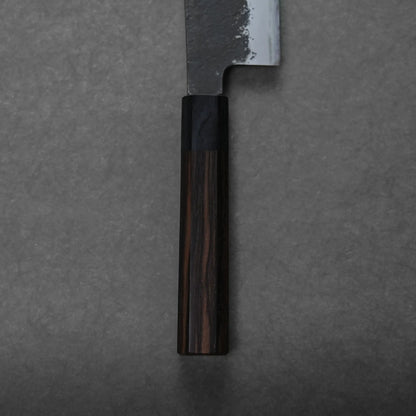 A close-up of a hakata knife with a dark wooden handle and a partially visible blade on a gray, textured surface.