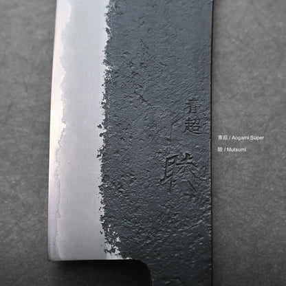 Close-up view of a Japanese hakata knife blade, featuring a textured, dark forged upper section and a polished silver edge. Japanese kanji characters are engraved on the blade. Text on the right reads Aogami Super and Mutsumi.