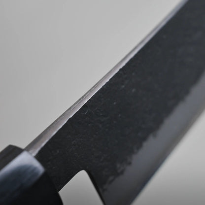 Close-up view of a hakata knife blade, showing the spine finish against a neutral gray background.