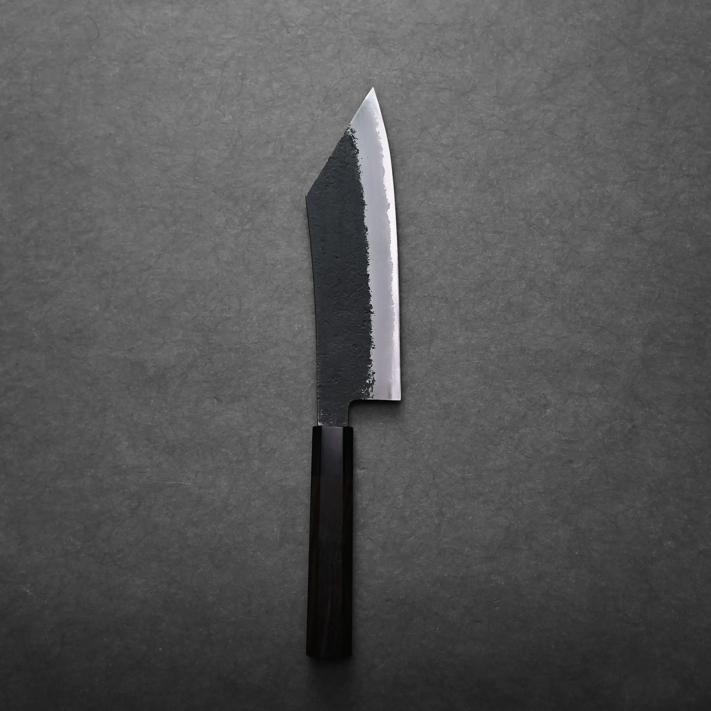 A single hakata knife with a dark wooden handle and a partially blackened, straight-edged blade is placed on a gray textured surface.