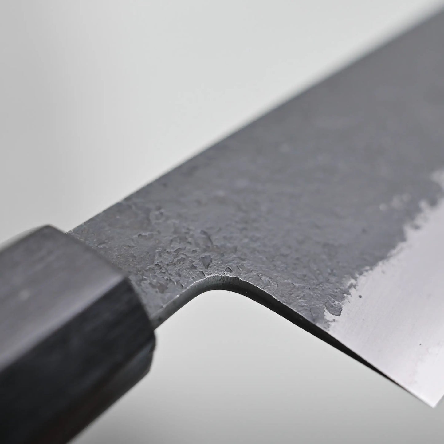 Close-up view of the choil finish of a kiritsuke gyuto knife against a plain background.