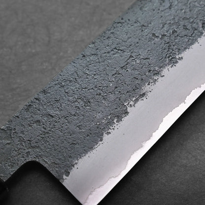 Close-up of a kiritsuke Japanese chef's knife blade, featuring a textured, matte upper section and a smooth, polished lower cutting edge against a dark background.