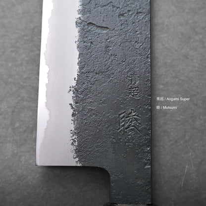 Close-up of a kiritsuke gyuto blade, showing a distinct textured and polished contrast. Japanese characters are engraved, with additional text reading “青超 / Aogami Super” and “睦 / Mutsumi”.