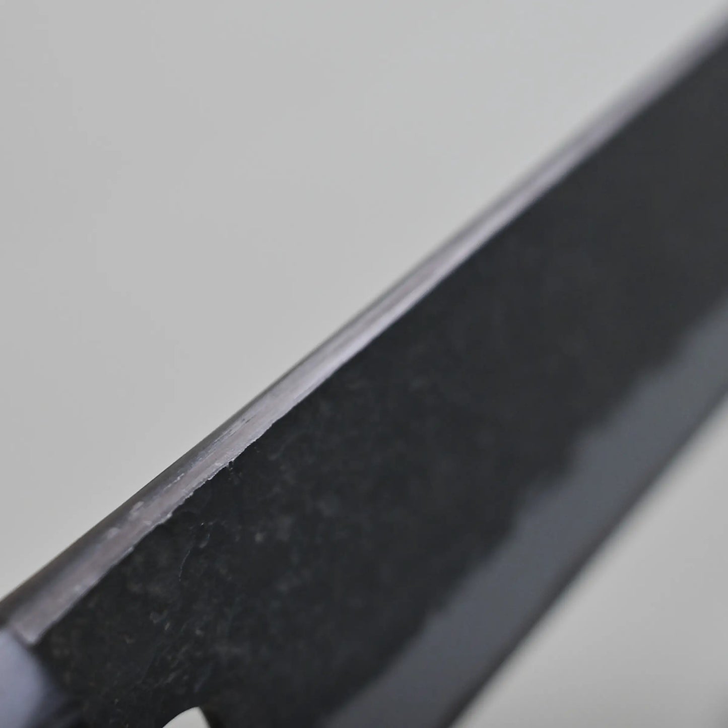 Close-up view of the spine finish of a kiritsuke gyuto blade against a light gray background.