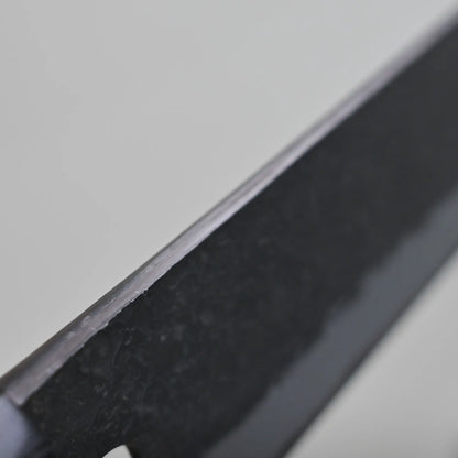 Close-up view of the spine finish of a kiritsuke gyuto blade against a light gray background.