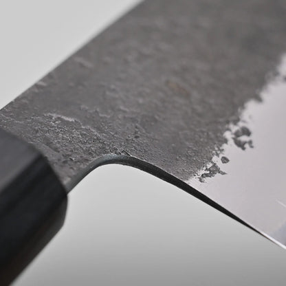 Close-up of a nakiri knife blade showcasing the choil finish with a wooden handle partially visible.