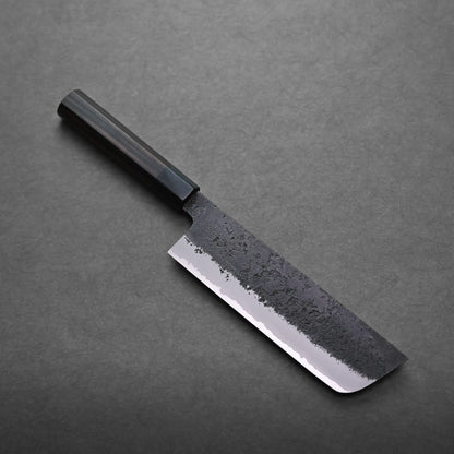 A Japanese vegetable knife with a black handle and a dark, textured blade lies on a gray surface. The nakiri knife features a straight edge and a shiny, polished lower section.