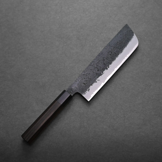A Japanese vegetable knife with a dark wooden handle and a rectangular, partially textured blade lies on a dark, flat surface.