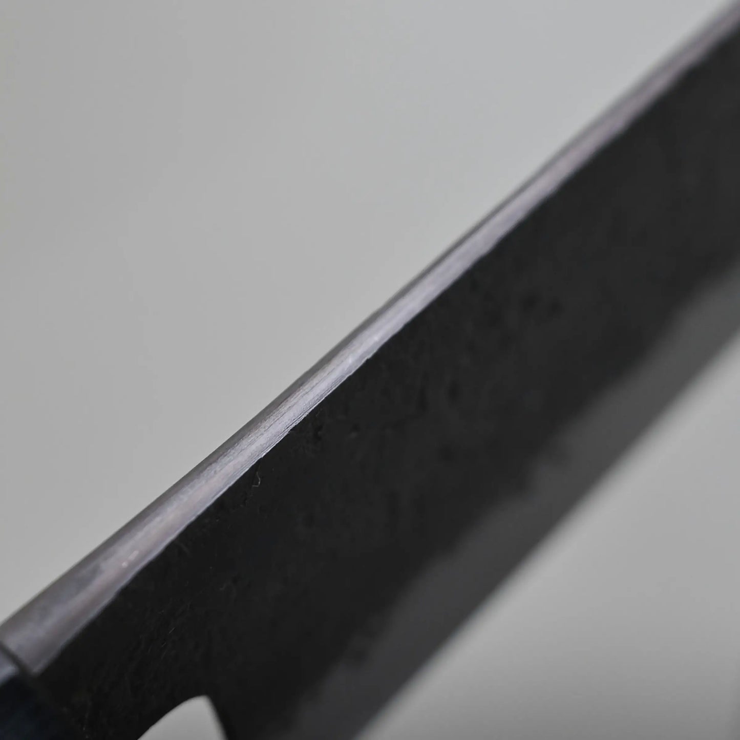 Close-up view of the spine finish of a Japanese vegetable knife against a plain, light-colored background.
