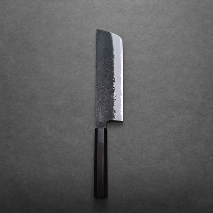 A Japanese vegetable knife with a dark wooden handle and a rectangular, partially textured steel blade is positioned vertically on a gray surface.