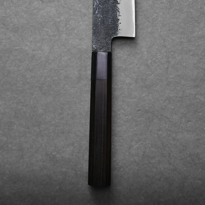 A close-up of a Japanese slicing knife with a dark wooden handle and a partially textured metal blade, positioned vertically on a gray textured surface.