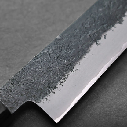 Close-up of a Japanese slicing knife blade with a textured, dark upper section and a smooth, sharp edge, placed on a dark gray surface.