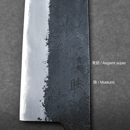 Close-up of a Hinoura gyuto blade highlighting the contrast between polished and textured steel, with Japanese characters engraved alongside product information text reading Aogami super and Mutsumi to the right.