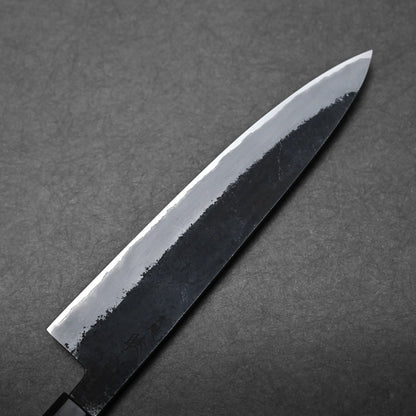 A close-up view of a Japanese chef's knife, featuring a dark, textured blade and polished finish, placed on a dark, textured surface.