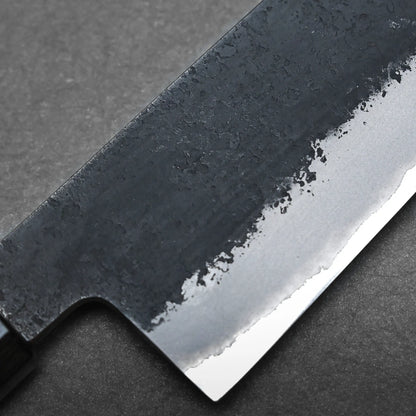 Close-up of a Hinoura gyuto Japanese chef's knife featuring a dark, textured blade with a polished finish, shown against a dark background.