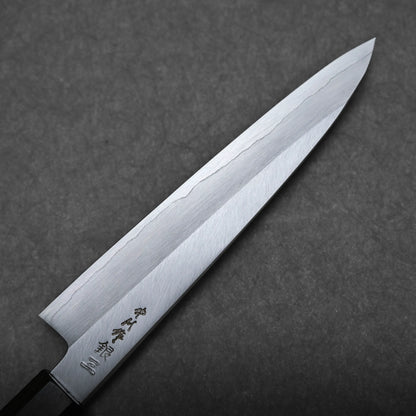 A close-up of a Japanese utility knife with a sharp, polished blade featuring subtle engraving and a visible hamon line, set against a gray textured background.