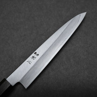 A close-up view of a Japanese utility knife, or petty knife, with a sharp, pointed blade and Japanese characters engraved near the handle, set against a dark, textured background.