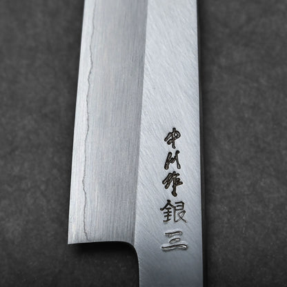 Close-up of a Japanese utility knife blade with a visible wavy pattern and engraved Japanese characters near the edge, set against a dark background.