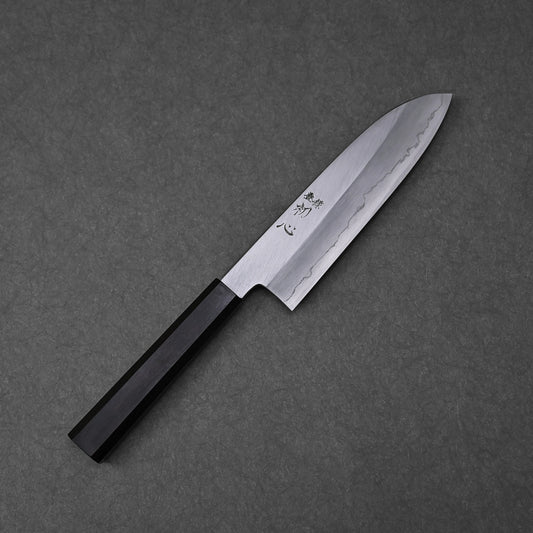 Santoku knife featuring a patterned blade with vertically engraved kanji characters near the handle; paired with a black handle and photographed to emphasize steel texture and traditional craftsmanship.