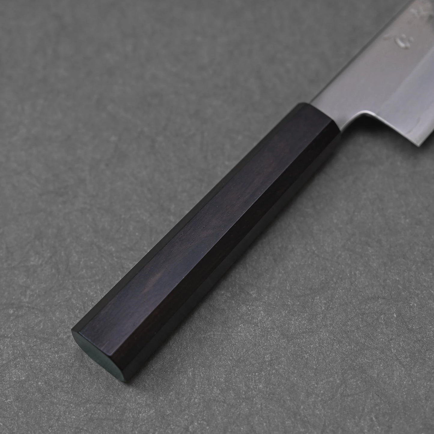 Close-up of a mono octagonal ebony handle on a santoku knife; photographed to highlight the handle’s dark tone, clean geometry, and refined wood texture.
