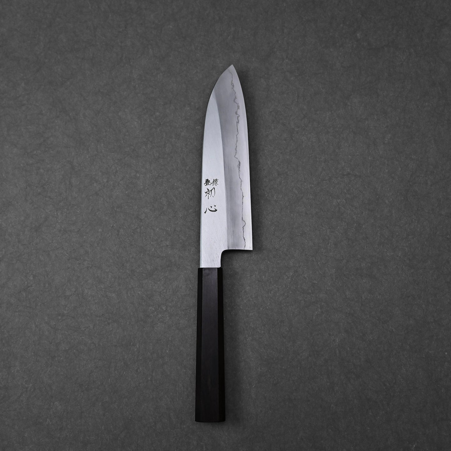 Santoku knife shown in full profile with vertically engraved kanji characters near the handle; photographed in a vertical orientation to highlight the blade and handle together.
