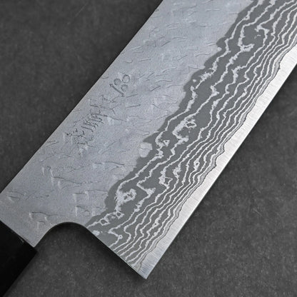 Close-up of a Nigara tsuchime damascus VG10 bunka 180mm knife, showcasing its hammered damascus blade with engraved markings near the handle, displayed on a dark, textured surface.