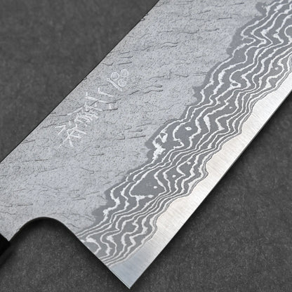 Close-up of the Nigara tsuchime damascus VG10 kiritsuke gyuto 210mm blade, showing intricate patterns, a sharp edge, and engraved markings against a dark background.