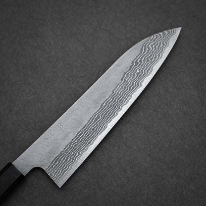 A close-up of the Nigara Hamono Nigara tsuchime damascus VG10 gyuto 210mm knife, showcasing its wavy-patterned blade on a dark textured background.