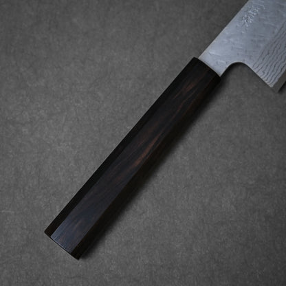 A close-up of the Nigara Hamono Nigara tsuchime damascus VG10 gyuto 210mm shows its richly grained dark wooden handle and part of the hammered damascus blade, set on a gray surface.
