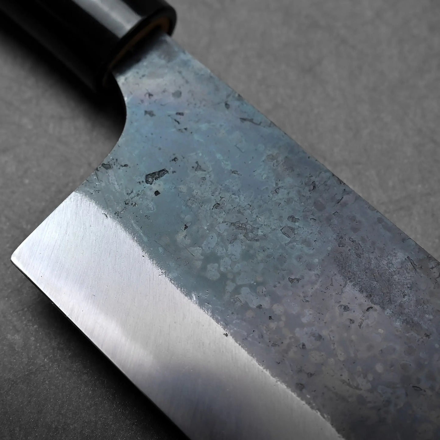 Rectangular blade with visible marks and a dark finish; Japanese knife shown in close-up, likely a nakiri.