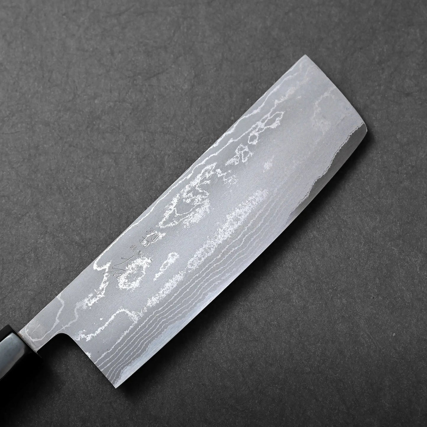 A close-up shows a Japanese knife, specifically a nakiri, with a straight-edged rectangular blade and dark handle.