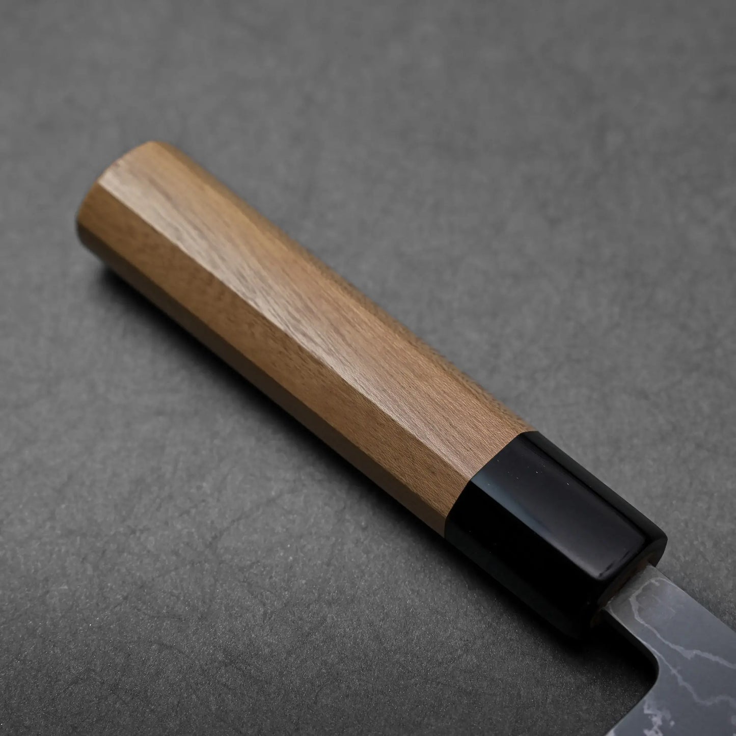Close-up shows the wooden handle and black bolster of a Japanese knife, nakiri type, with no blade details visible.