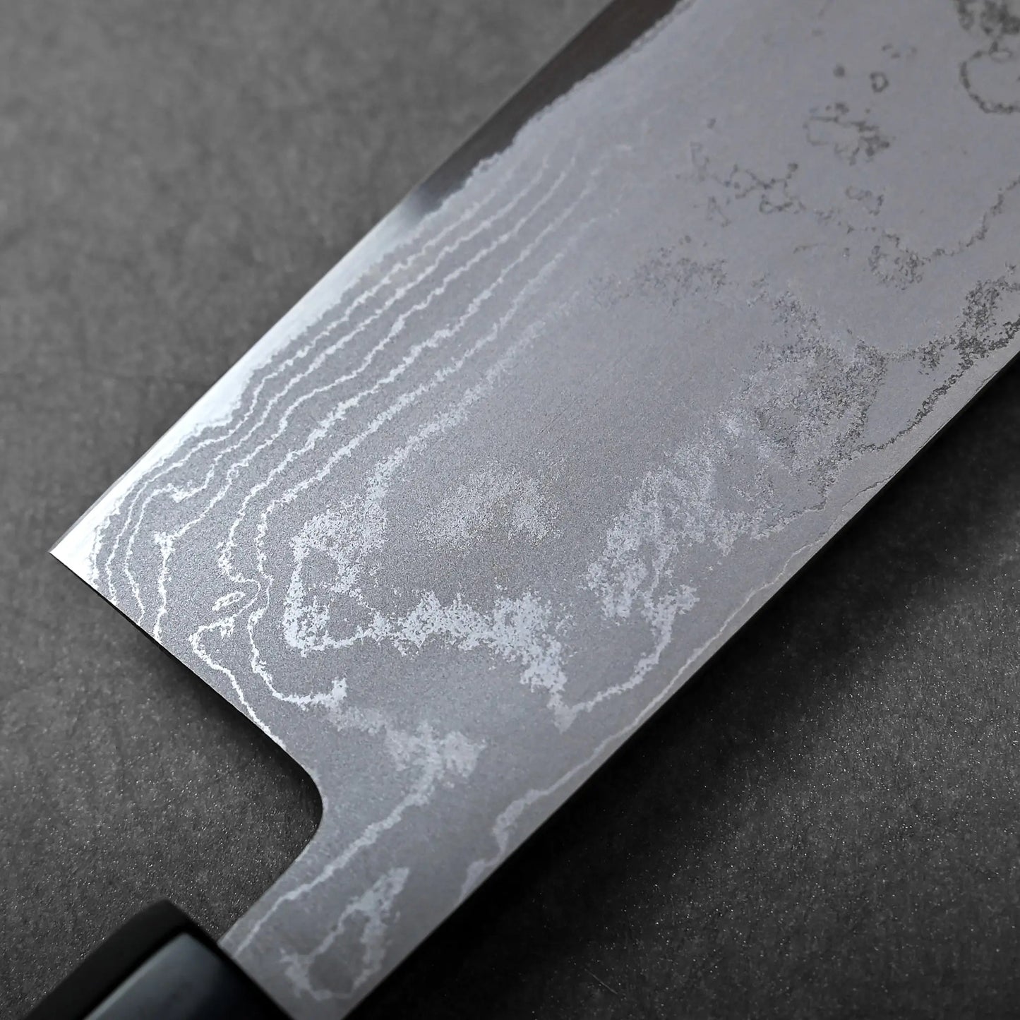 Close-up of nakiri blade with straight edge, squared tip, Japanese knife featuring visible Damascus steel pattern.