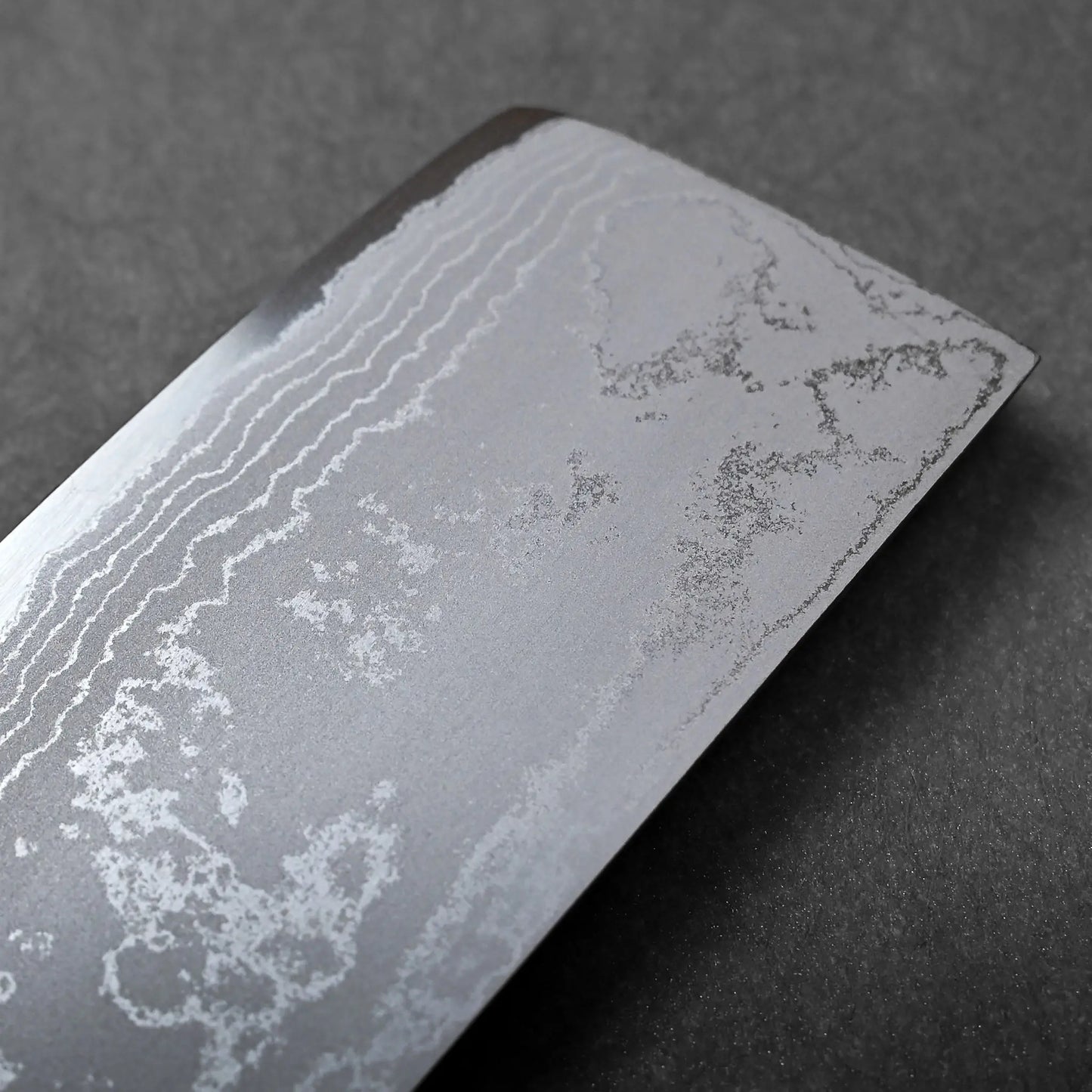 The flat-edged, rectangular blade of this Japanese knife displays a visible wavy Damascus steel pattern up close.