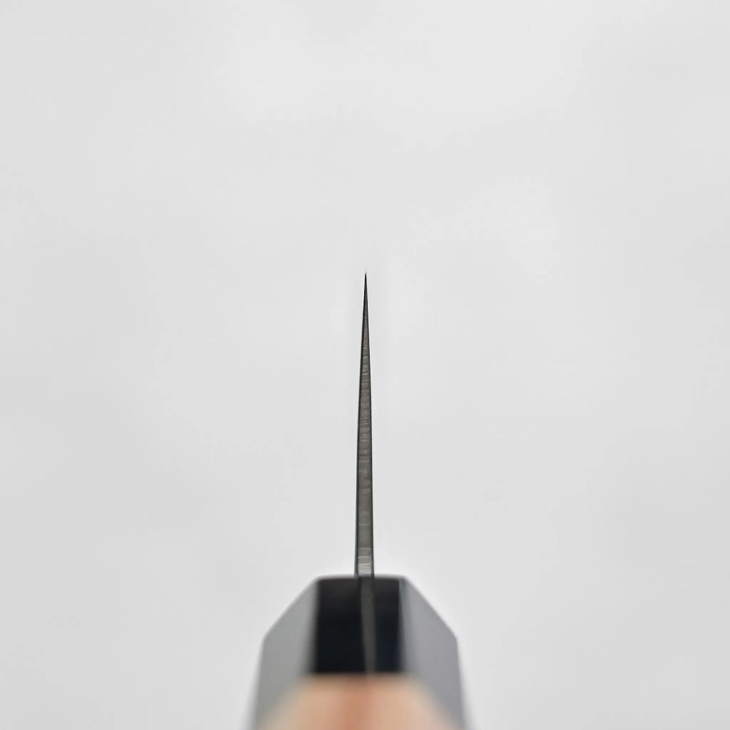 Choil shot of a Japanese knife, santoku type, showing visible curve and damascus cladding pattern in close-up view.