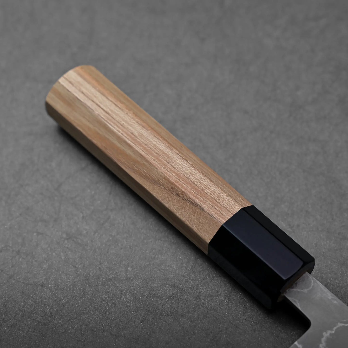 Close-up of a Japanese knife showing santoku blade shape with damascus cladding and a black bolster.