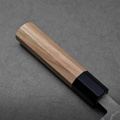 Close-up of a Japanese knife showing santoku blade shape with damascus cladding and a black bolster.