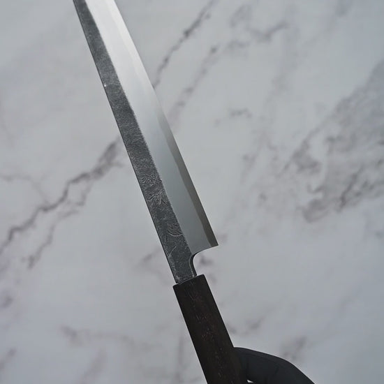 Short video showcasing an aogami#2 kurouchi yanagiba knife from Hatsukokoro rotating to display the blade, handle, and overall craftsmanship from multiple angles.