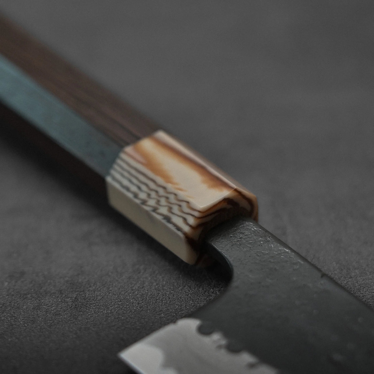 Close-up of a gyuto featuring a dark damascus blade and a wooden handle.