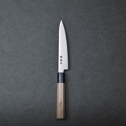 A single Sakai petty knife with a wooden handle and a pointed blade rests on a dark gray surface. Japanese characters are engraved on the stainless blade.