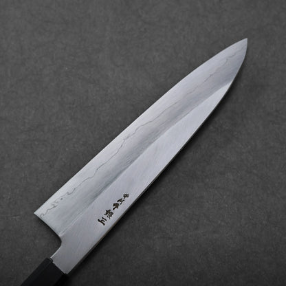 A Japanese chef's knife with a polished steel blade featuring wave-like patterns and Japanese characters near the handle rests on a dark textured surface.