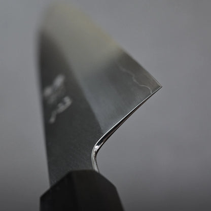Close-up of the sharp edge and tip of a gyuto knife with a black handle, set against a plain grey background. The blade shows a subtle wavy pattern near the edge.