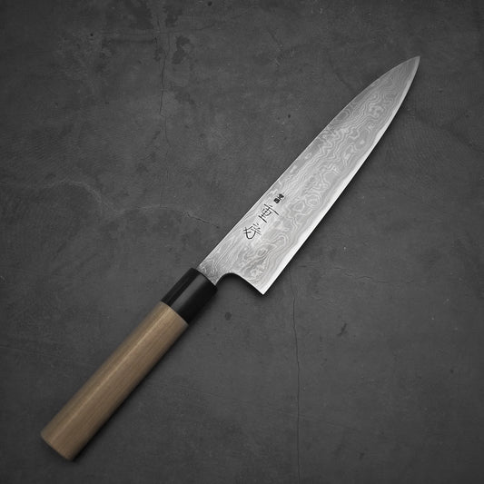 Top-down view of a 210mm gyuto with Damascus finish and light wood handle, placed on a dark surface. Shigefusa kitaeji model.