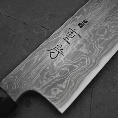 A close-up of a knife's blade, showcasing its unique Damascus steel pattern and distinct kanji character engravings. It rests on a dark background.