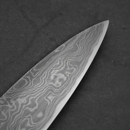 Close-up of a damascus steel knife blade on a dark background showing the tip area